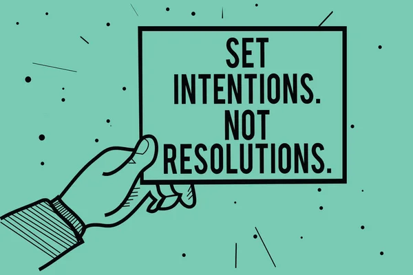Text sign showing Set Intentions. Not Resolutions.. Conceptual photo Positive choices for new start achieve goals Man hand holding paper communicating information dots turquoise background