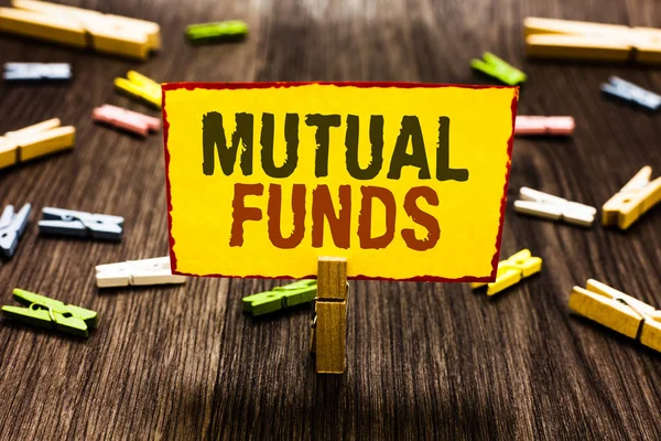 Handwriting text writing Mutual Funds. Concept meaning An investment program funded by shareholders Individual Stocks Clothespin holding yellow paper note several clothespins wooden floor.