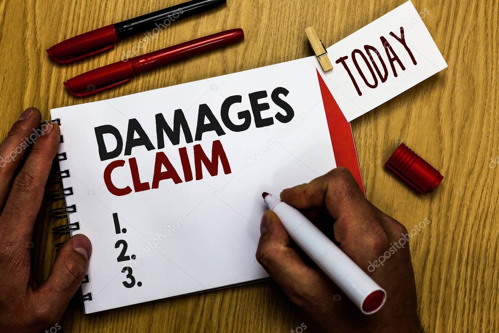 Handwriting text writing Damages Claim. Concept meaning Demand Compensation Litigate Insurance File Suit Man holding marker notebook clothespin reminder wooden table cup coffee.