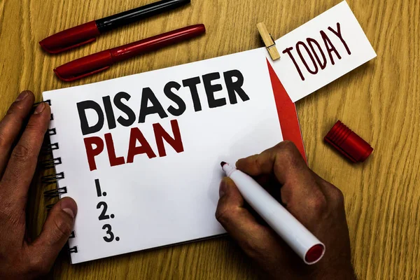 Handwriting text writing Disaster Plan. Concept meaning Respond to Emergency Preparedness Survival and First Aid Kit Man holding marker notebook clothespin reminder wooden table cup coffee.