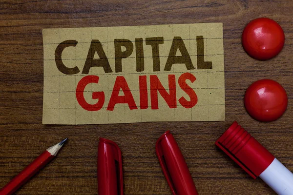 Handwriting text writing Capital Gains. Concept meaning Bonds Shares Stocks Profit Income Tax Investment Funds Paperboard markers pencil wooden background communicating ideas red balls.