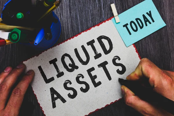 Conceptual hand writing showing Liquid Assets. Business photo text Cash and Bank Balances Market Liquidity Deferred Stock Man holding marker paper clothespin reminder cup marker wood table. — Stock Photo, Image