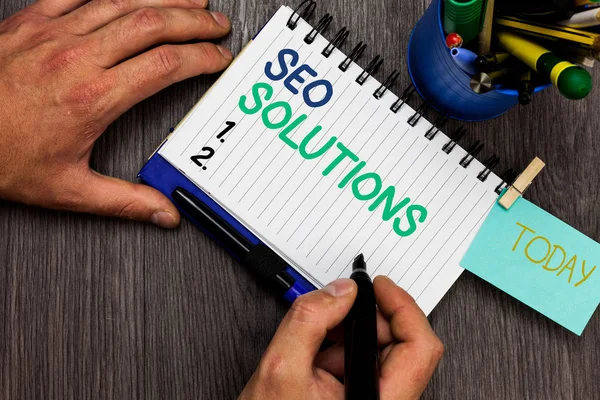 Conceptual hand writing showing Seo Solutions. Business photo showcasing Search Engine Result Page Increase Visitors by Rankings Man holding marker notebook reminder cup markers wood table. — Stock Photo, Image