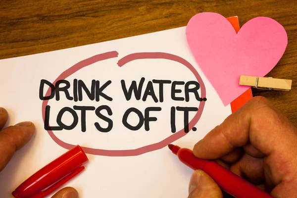 Handwriting text Drink Water. Lots Of It. Concept meaning drinking liquids to keep our body in great status Human hand retain red pen circled black words paper hook rivet pink heart.