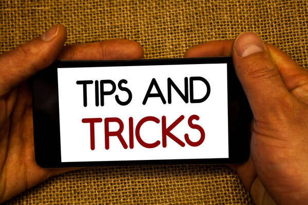 Conceptual hand writing showing Tips And Tricks. Business photo text Suggestions to Make things easier Helpful Advices Solutions Man holding cell phone screen black red letters wicker background.