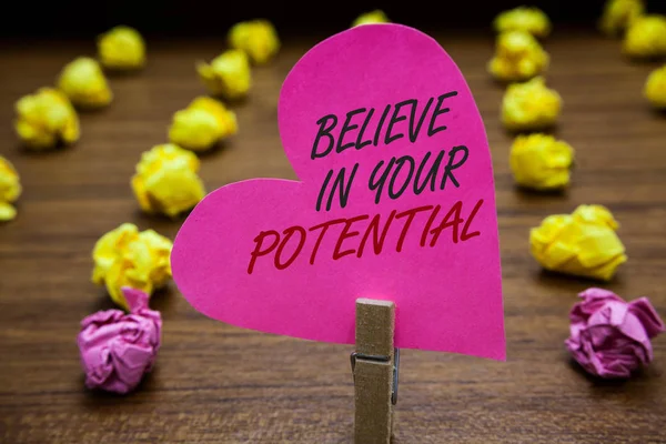 Text sign showing Believe In Your Potential. Conceptual photo Have self-confidence motiavate inspire yourself Paperclip hold pink heart with text blurry paper lobs on wooden floor.