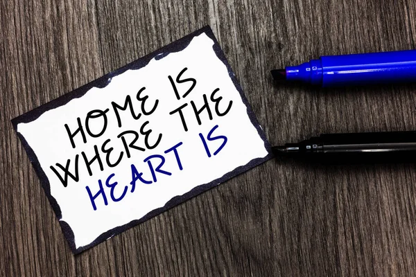 Word writing text Home Is When The Heart Is. Business concept for Your house is where you feel comfortable and happy Black bordered page with texts laid black and blue pen on wooden floor.
