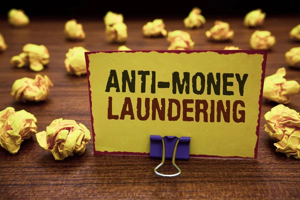 Handwriting text writing Anti Money Laundering. Concept meaning stop generating income through illegal actions Yellow sticky card clipped text notice crumpled paper balls wood table.
