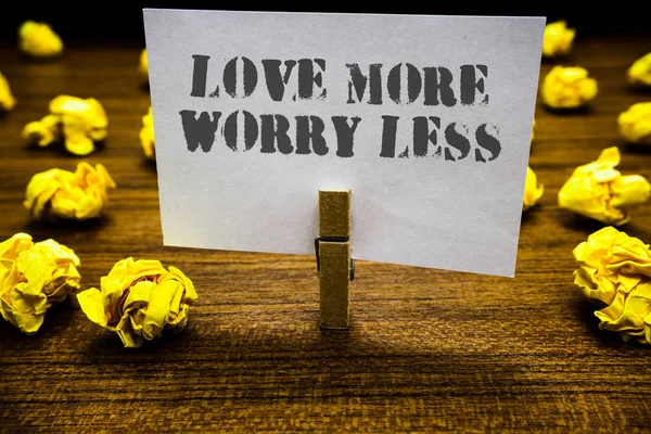 Text sign showing Love More Worry Less. Conceptual photo Have a good attitude motivation be lovable enjoy life Paperclip grip white page with grey text woody floor laid blurry yellow lob.