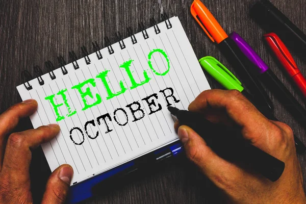 Handwriting text writing Hello October. Concept meaning Last Quarter Tenth Month 30days Season Greeting Man holding marker notebook paper communicating ideas Wooden background.