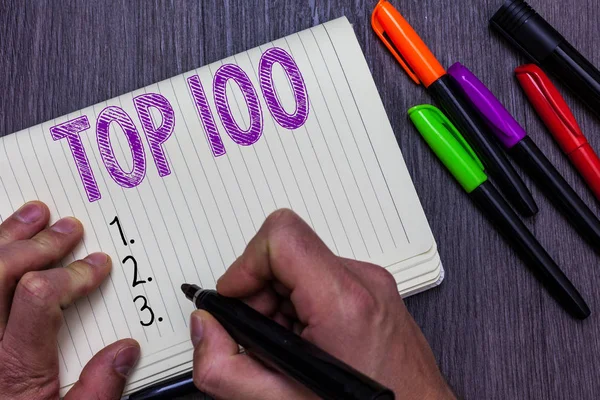 Text sign showing Top 100. Conceptual photo List of best products services Popular Bestseller Premium high rate Man holding marker notebook paper communicating ideas Wooden background. — Stock Photo, Image