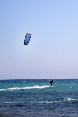 Sörfçü çekiş uçurtma uçuran bir Wakeboard üzerinde. Binici içinde ayakta ve sörf tahtası üzerinde dengeleme Wetsuit. Mavi su ve Clear Sky. Su sporları macera fikirler.