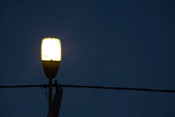 Lanterne de rue extérieure avec bras unique incurvé en acier. Luminaire pour lampadaire illuminant le ciel bleu foncé. Fil de câble à travers et poteau à l'arrière . — Photo