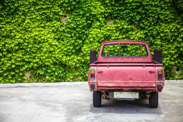 Rustic Red Pickup Parked Alone in Open Lot. Abandoned Old Truck with Stake Rail Board Facing a Shrubbery Wall. Open Delivery Vehicle Shot at Rear End View. — Stock Photo, Image