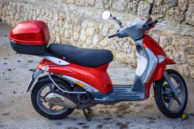 Bir kırmızı motosiklet ile düz zemin Kurulu adım üzerinde bir kirli Park yeri. SideView atış motosiklet kask depolama Case eski bir taş bakan ile duvara döşeli.