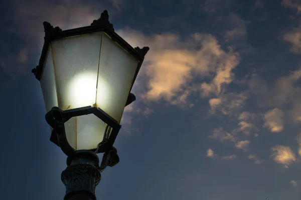 Primer plano de estilo victoriano Street Lantern con cubierta de vidrio ahumado y bombilla iluminada. Vista hacia arriba de la lámpara exterior hecha de fundición de hierro bajo el cielo nublado tenue . —  Fotos de Stock