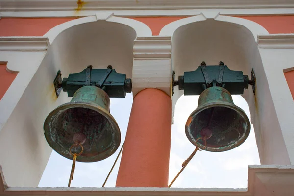 Two Old Rusty Antique Bells Hanging from the Church Open Arched Belfry. Percussion Instrument Producing Sound when Struck. Chapel Toll Tower has New Paint.