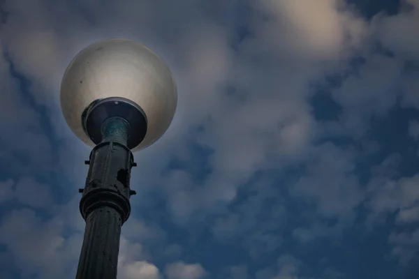 Vista angular del poste de la lámpara al aire libre de pie bajo el cielo nublado oscuro. Primer plano de One Street Lantern con bombilla redonda de globo ahumado y agujero en poste fundido de hierro . —  Fotos de Stock