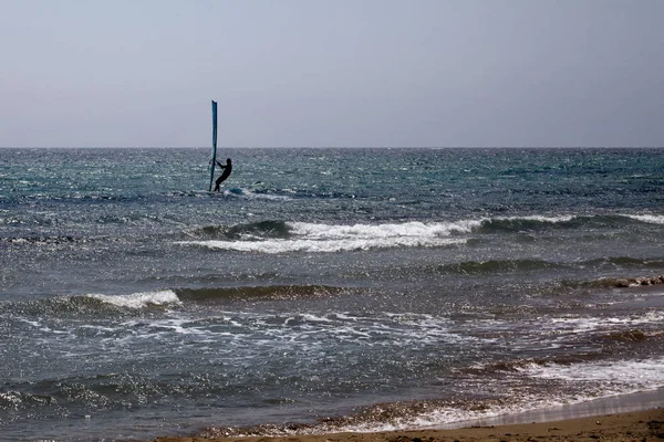 Wave Rider Windsurfing v oceánu. Modrá voda a jasná obloha. SideView daleko zastřelil Surfer balancování na Surfing Board s plachtou. Venkovní sportovní dobrodružství. — Stock fotografie