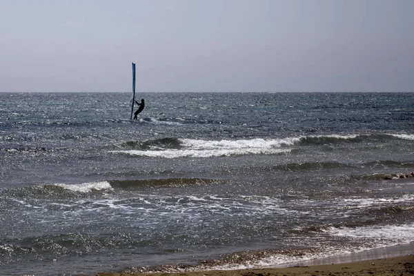 Surfař v oceánu balancování na windsurfingu desky. Blue Wave a jasná obloha. Jezdec režii stěžně plachtou proti větru. Vodní Sport venkovní dobrodružství. — Stock fotografie