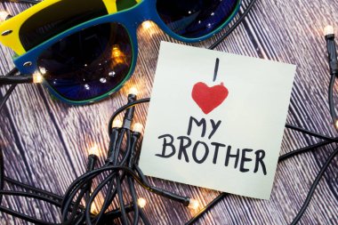 Işıklı küçücük Led Stringlight ahşap yüzeyine dağılmış. İki renkli güneş gözlükleri-ışık yansıtan ile. El yazısıyla yazılan mesaj Brother için aşk ifade.