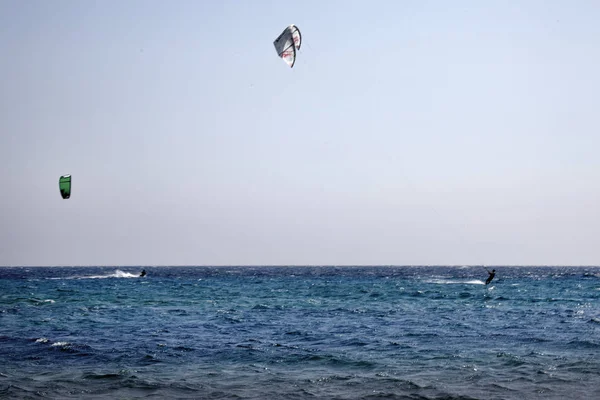 Волновые Всадники занимаются кайтсерфингом на волнистом голубом океане. Серфингисты, летающие на мощном воздушном змее по водной поверхности в один прекрасный день. Водный спорт под открытым небом . — стоковое фото