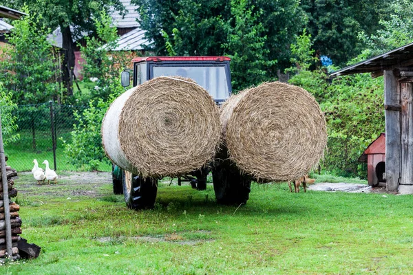 Traktor med stora runda balar av halm. Byn fungerar med traktor. Hö balar produktion på byn. Byn landskap med peasent verktyg i trädgården. — Stockfoto