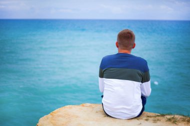 Siyah pantolon ve gömlek genç hiker uçurumun kenarında oturan ve puslu tepelik Vadisi körük için arıyorsunuz