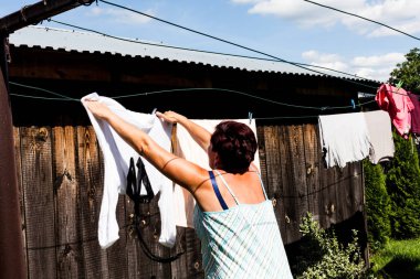 Giysi güneşli bir günde dizginin üzerinde asılı bir kadının arkadan görünüm odaklı. Metal dize ve klipleri giysi kurutma sırasında güvenliğini sağlama. Kentsel yaşam ve tipik ev tel.