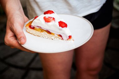 Bir dilim çilekli cheesecake gösterilen bir tabak tutan bir el. Üstte nefis seyir taze çilek. Tatlı yapımı hobi. Fırın ekmek ve hamur işleri fikirler.