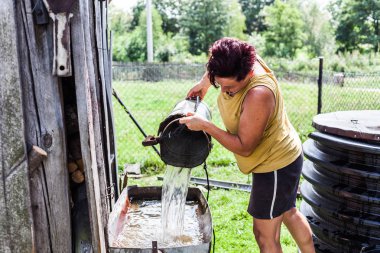 Ahır dışında sığ Havzası dolduruyor çalışkan anne. Doğal kuyudan su alma kadın. Tipik ev iş. Kırsal alan senaryo.