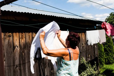 Beyaz kumaş güneşli bir günde dizginin üzerinde asılı bir kadının arkadan görünüm. Metal dize ve klipleri giysi kurutma sırasında güvenliğini sağlama. Kentsel yaşam ve tipik ev tel.