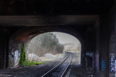 Birmingham, İngiltere - Mart 2018 tren yolu altında yıpranmış köprü tünel. Tuğla duvar kirli ve Vandalized var. Çakıl ve çevresinde kuru dal. Taze yaprakları sürünerek duvar.