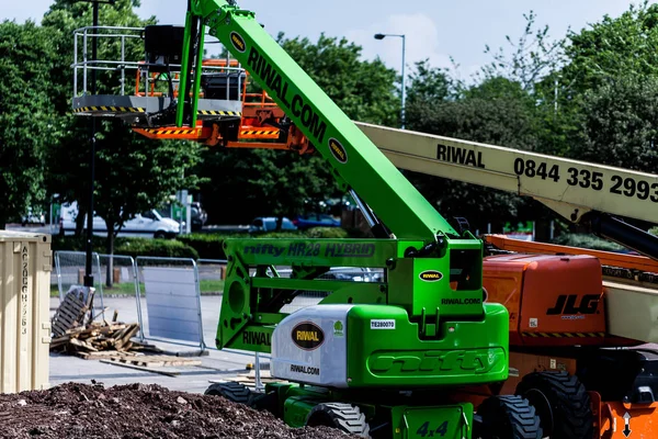 BIRMINGHAM, Royaume-Uni - Mars 2018 Deux élévateurs à flèche garés dans la rue avec plate-forme levée. Dalles de bois, clôtures et dépotoir de sol près de la machinerie. Arbres alignés en arrière-plan . — Photo