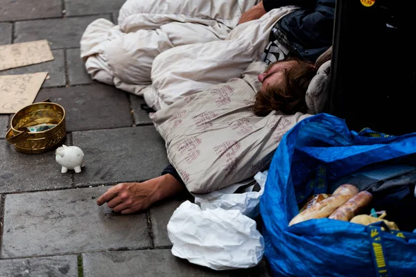Birmingham, İngiltere - Mart 2018 zor uyuyan eşyalarını ile soğuk kaldırımda yatarken. Kumbara geçenler tarafından verilen para için teneke kapsayıcı yanında. Evsiz dilenci bakım ihtiyacı.
