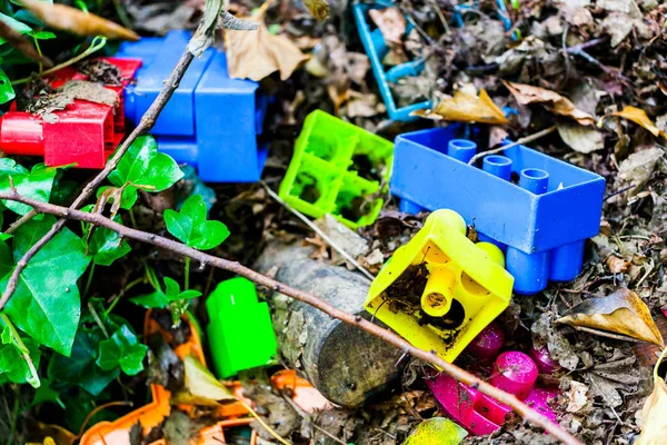 Colorful kids plastic cube toys thrown on the ground. Dirty kids toys on the soil.
