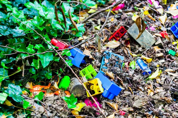 Colorful kids plastic cube toys thrown on the ground. Dirty kids toys on the soil.