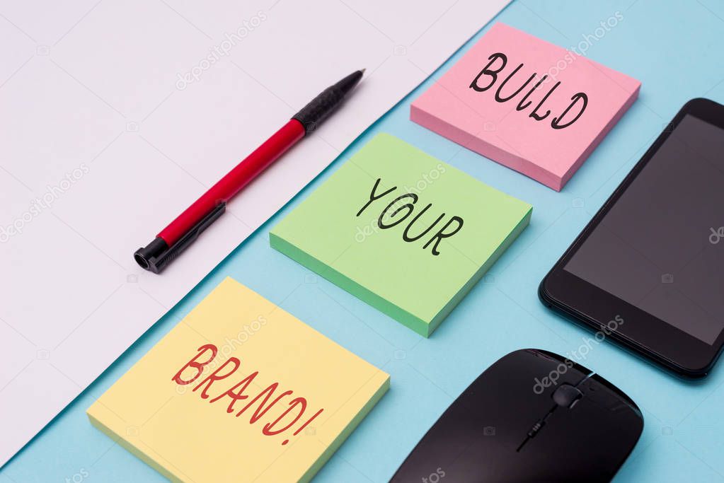 Word writing text Build Your Brand. Business concept for creates or improves customers knowledge and opinions of product Note papers and stationary plus gadgets placed sideways above backdrop.