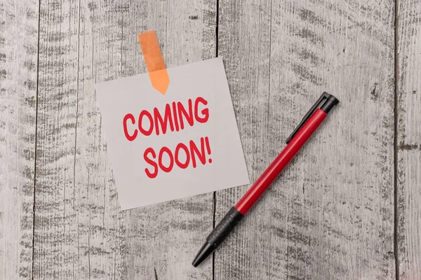 Text sign showing Coming Soon. Conceptual photo event or action that will happen after really short time One plain blank paper sheet and a pen attached with wooden textured table. — Stockfoto