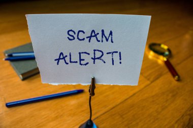 Scam Alert 'i gösteren not yazılıyor. İş fotoğraflarında sahtecilik yaparak kurbandan para kazanılıyor. Kağıt taban notasını hatırlatarak. Cam büyüteç elektronik cihaz..