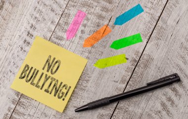 Zorbalık Yok 'u gösteren not yazıyorum. İş fotoğraflarının sergilenmesi çocuklar arasındaki agresif davranışları durdurur. Güç dengesizliği. Tahta masanın üstündeki ok çıkartmaları ve not kağıdı..