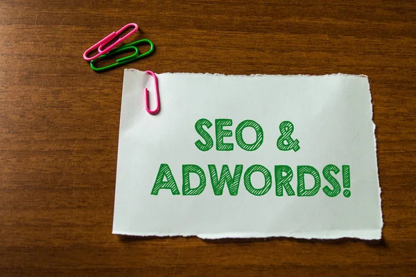 Texte d'écriture de mot Seo And Adwords. Concept d'affaires car ils sont les principaux outils composants de Search Engine Marketing Fermer papier stationnaire vierge tenir trois clips colorés couché table en bois . — Photo