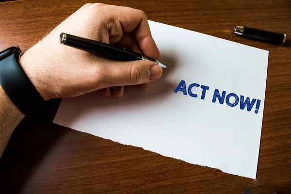 Conceptual hand writing showing Act Now. Business photo text do not hesitate and start working or doing stuff right away Man left hand watch paper ballpoint Pen cap lying wooden table. — Stock Photo, Image