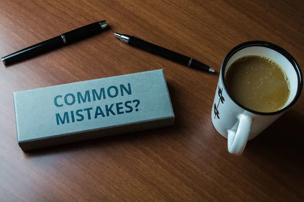 Word writing text Common Mistakes question. Business concept for repeat act or judgement misguided or wrong Upper close view two ball point pens case set coffee cup lying wooden table. — Φωτογραφία Αρχείου