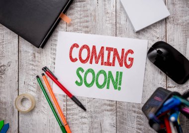 Yakında Geleceğini gösteren bir not yazıyorum. Kısa bir süre sonra, masa üzerinde kağıt kağıtlar olan kalem ve bilgisayar malzemesi içeren bir iş fotoğrafı gösterimi ya da eylem.