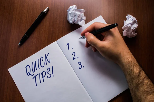 Text sign showing Quick Tips. Conceptual photo small but particularly useful piece of practical advice Upper close up view open notebook man hand pen paper balls wooden table. — Stock Photo, Image