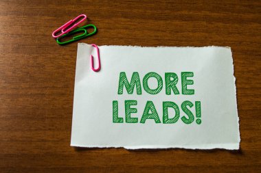Word writing text More Leads. Business concept for initiation of consumer interest or enquiry into product Close up blank stationary paper hold three colored clips lying wooden table.