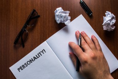 Kişiliği gösteren bir not yazıyorum. İş fotoğraflarının kombinasyon özellikleri bireysel karakterleri oluşturur. İnsan eli dinlenme kalemi açık, defter açık, yerde duran tahta masa gözlüğü okur..