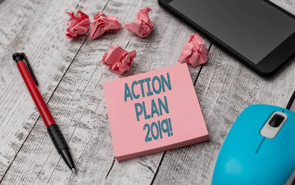Πινακίδα κειμένου που δείχνει το σχέδιο δράσης 2019. Εννοιολογική προτεινόμενη στρατηγική ή πορεία ενεργειών για το τρέχον έτος γράφοντας εξοπλισμό και χαρτί συν αποφάγια με gadget στο ξύλινο γραφείο. — Φωτογραφία Αρχείου