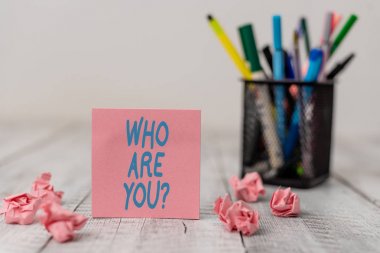 Text sign showing Who Are You Question. Conceptual photo asking about someone identity or demonstratingal information Set of plain note paper with scraps and stationary on the wooden table.